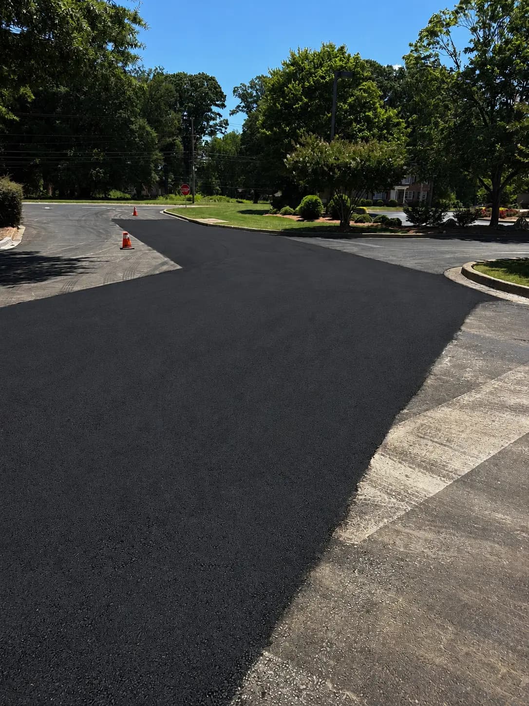New asphalt drive lane meeting a concrete apron, with landscaped islands and a stop sign
