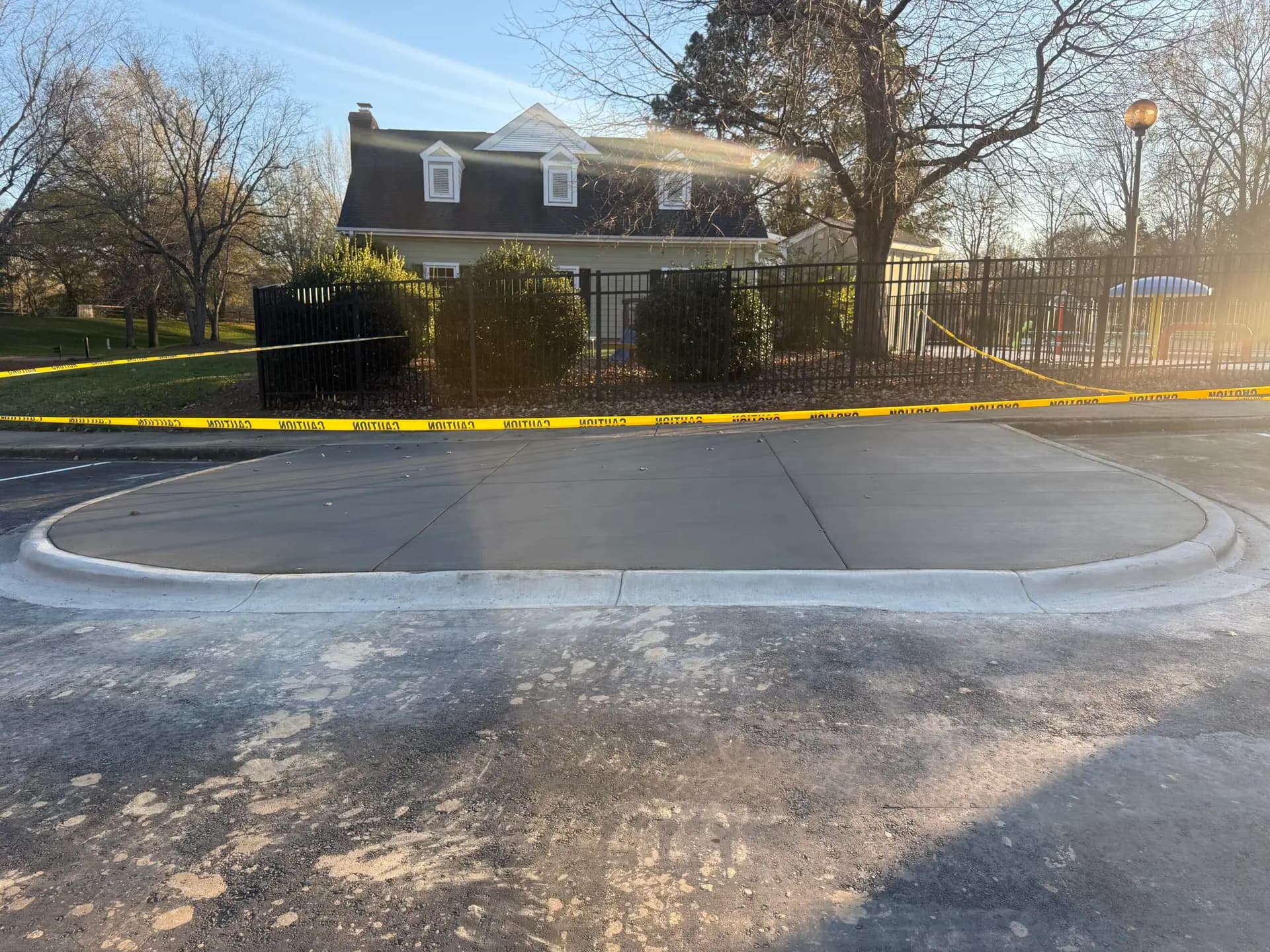 New concrete apron and curb at a fenced property, closed off with caution tape
