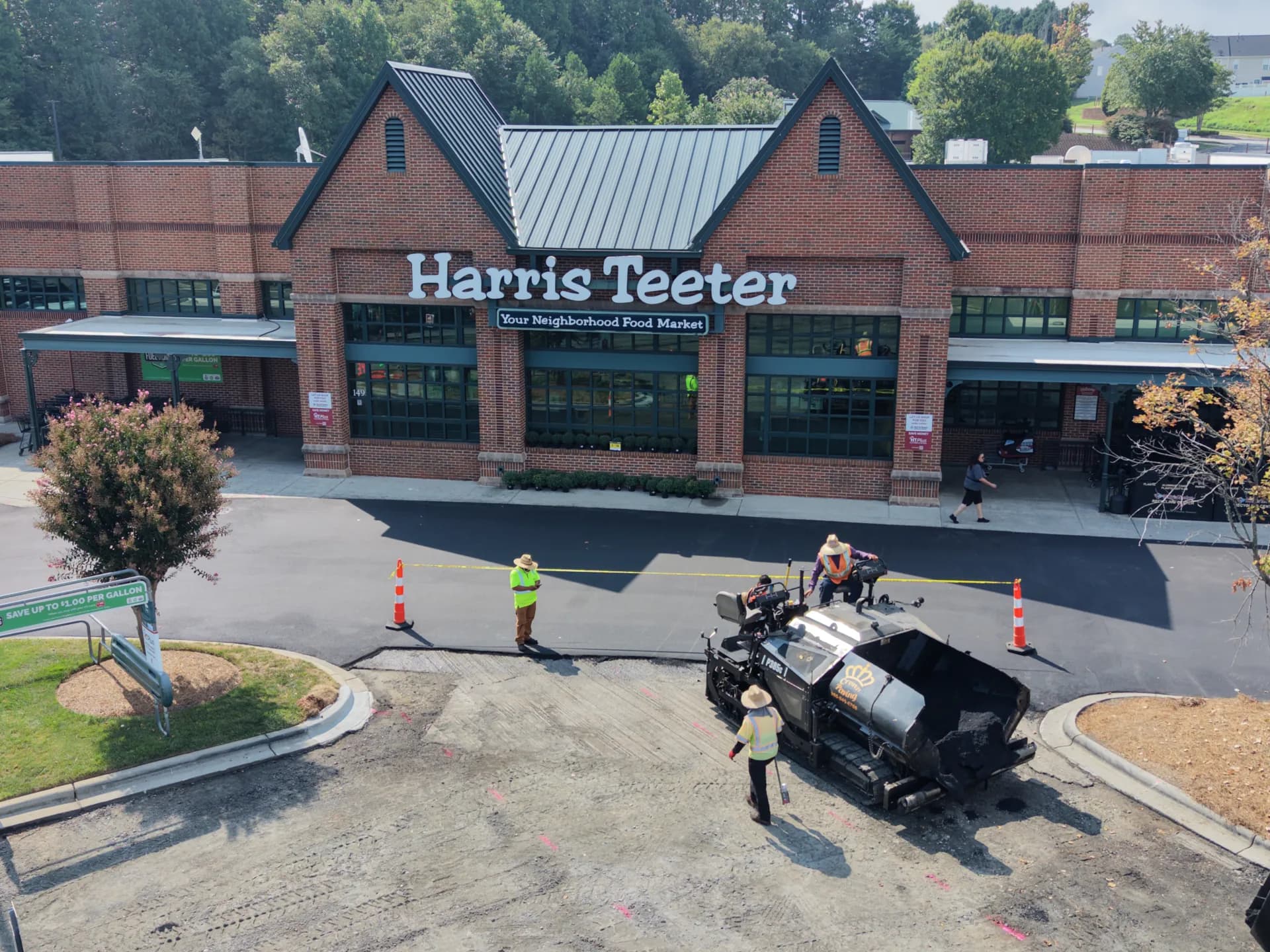 Crown Paving paver laying a fresh asphalt mat across the drive lane at a Harris Teeter store, with the milled section still open ahead of it