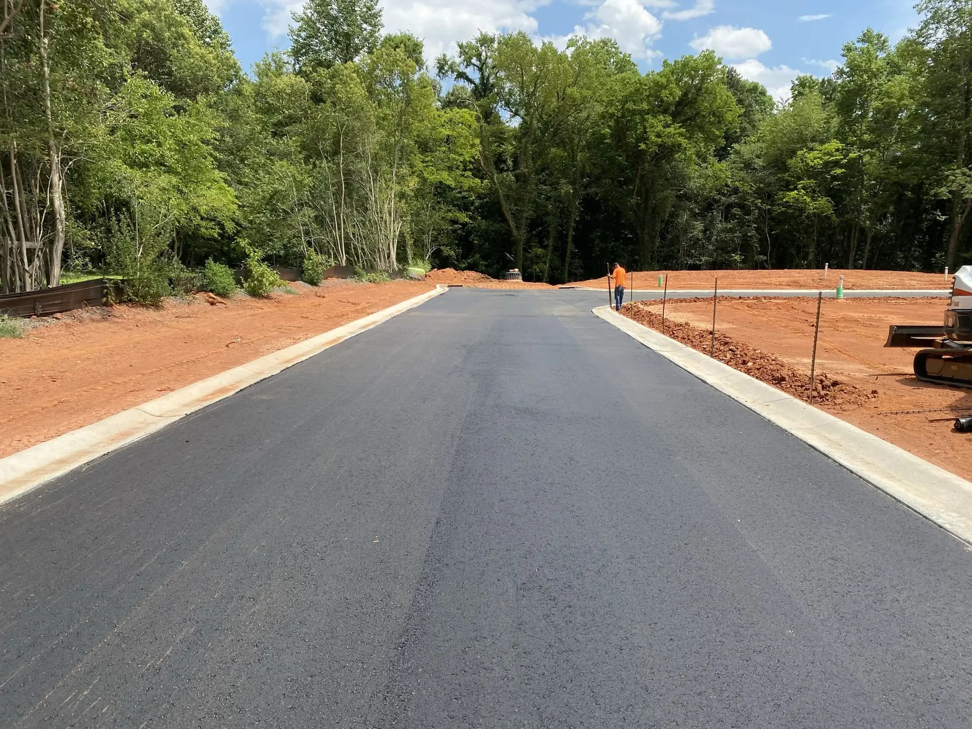 Newly paved roadway with concrete curb and gutter on both sides, still under construction