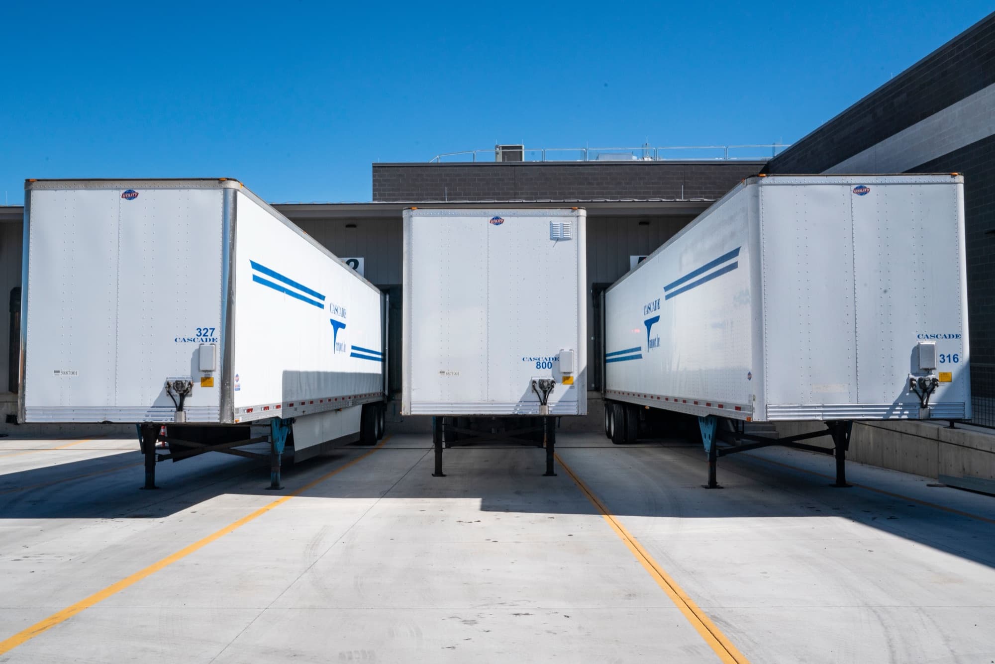 Three trailers backed into loading docks on a concrete apron marked with yellow lane lines