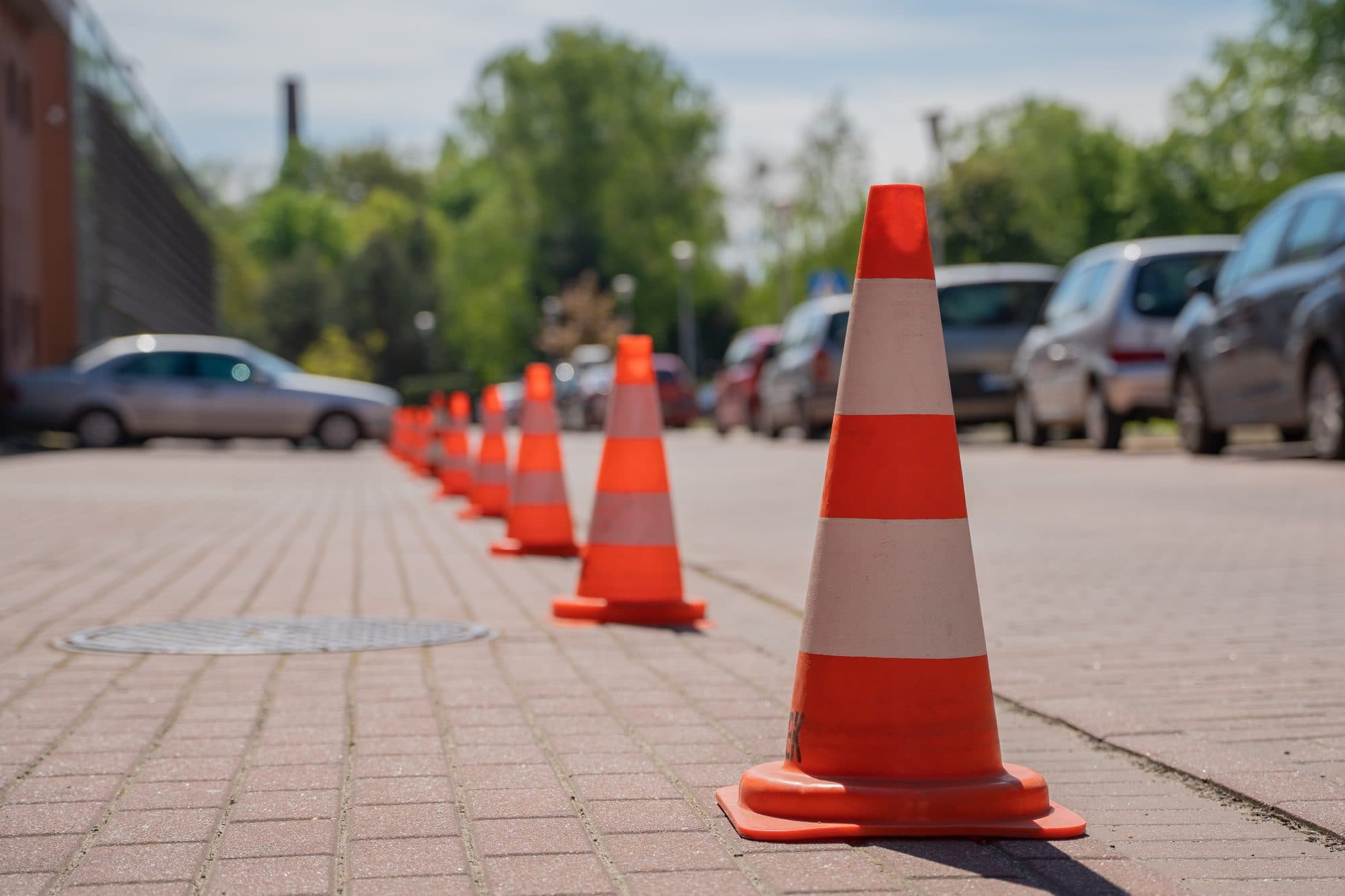A row of traffic cones closing off parking spaces beside parked cars